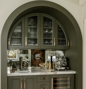 Painted green bar nook set inside an arched wall opening, with reeded-glass upper doors following the arch