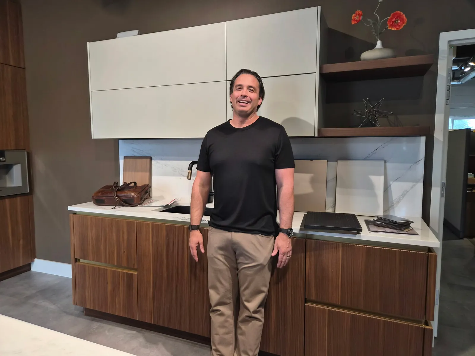 Two members of the Colorado Modern Kitchens team holding their dogs in front of a Pronorm wine display in the showroom