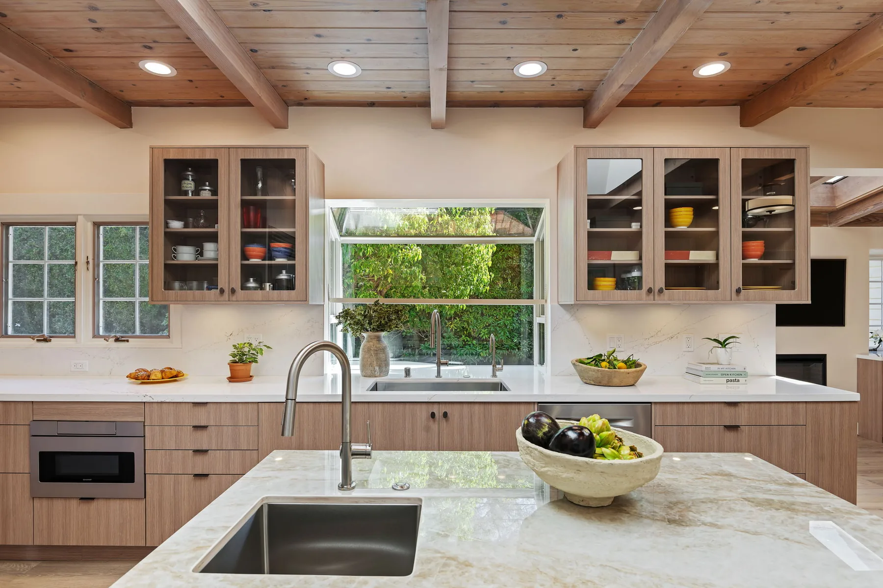 Garden window and glass-front upper cabinets framing the main sink