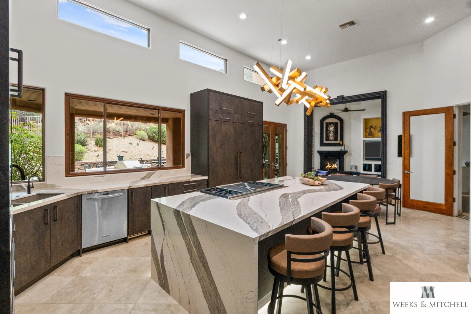 Open-plan view from the kitchen island across to the family room fireplace, Pronorm Dark Steel tall cabinets framing desert views through clerestory windows