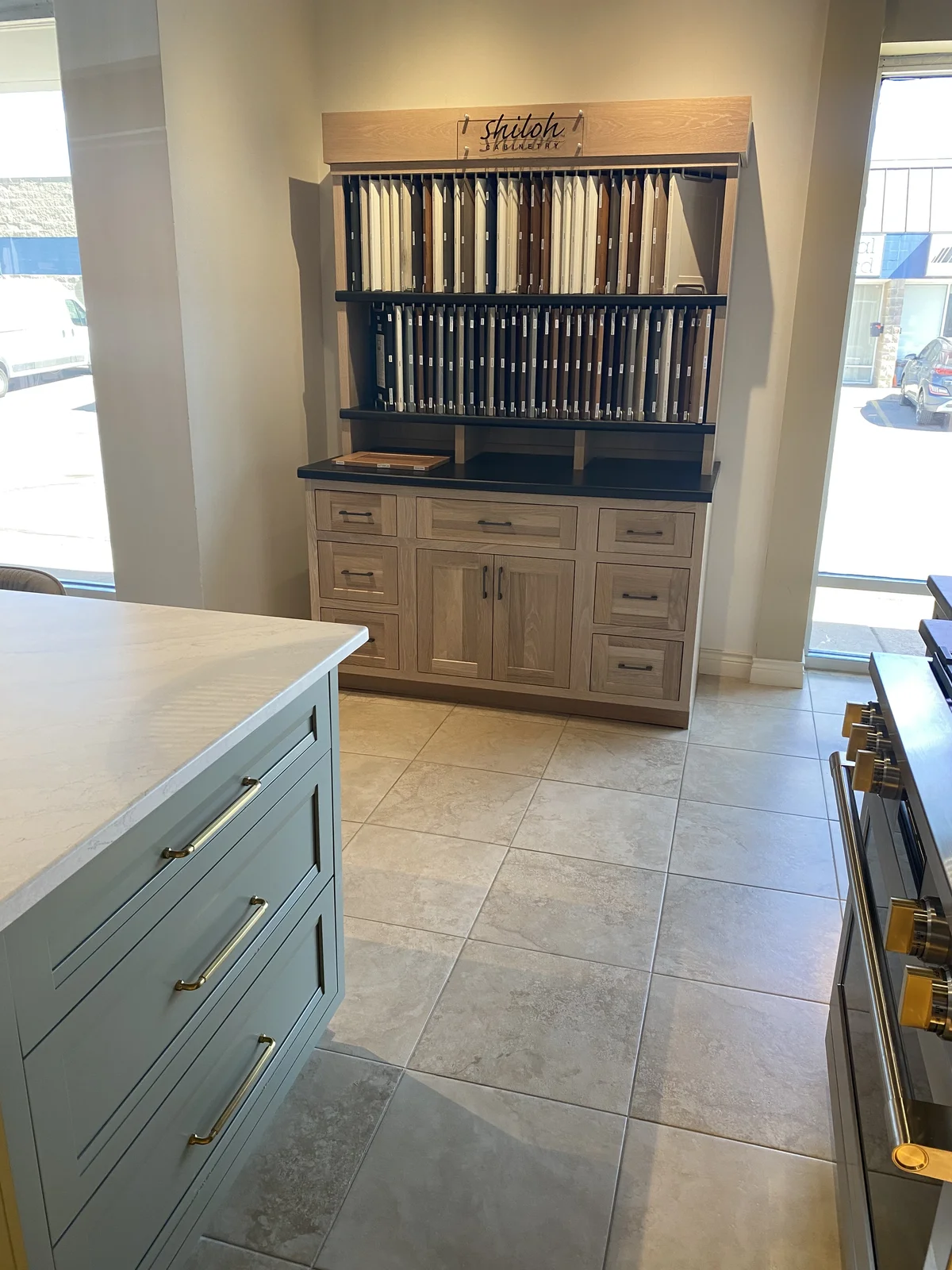 Shiloh Merchandiser display unit — a white oak hutch with the Shiloh Cabinetry sign at top, two rows of vertical door samples in painted and stained finishes, finish chips on the lower shelf, and a small Shiloh shaker base cabinet with quartz counter underneath