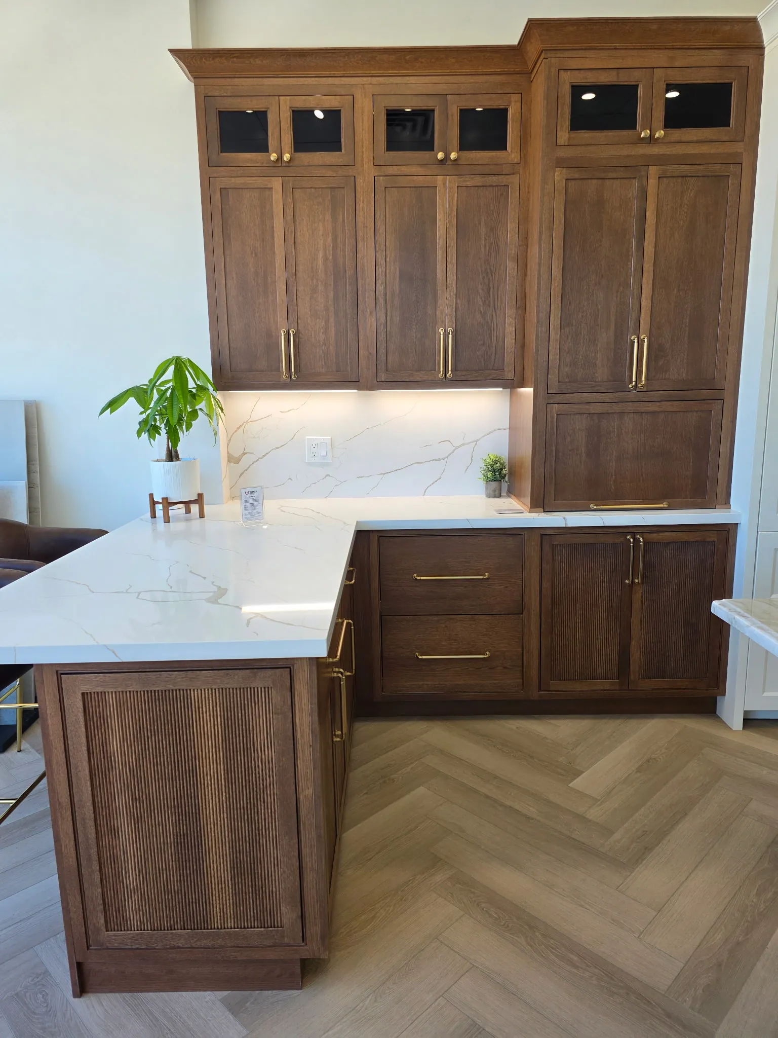 Wolf Renovations Shiloh Quarter Sawn White Oak kitchen in the Braun finish — shaker uppers with glass-front transom panels, Malibu Reeded base doors, antique-brass bar pulls, marble counter, herringbone wood floor