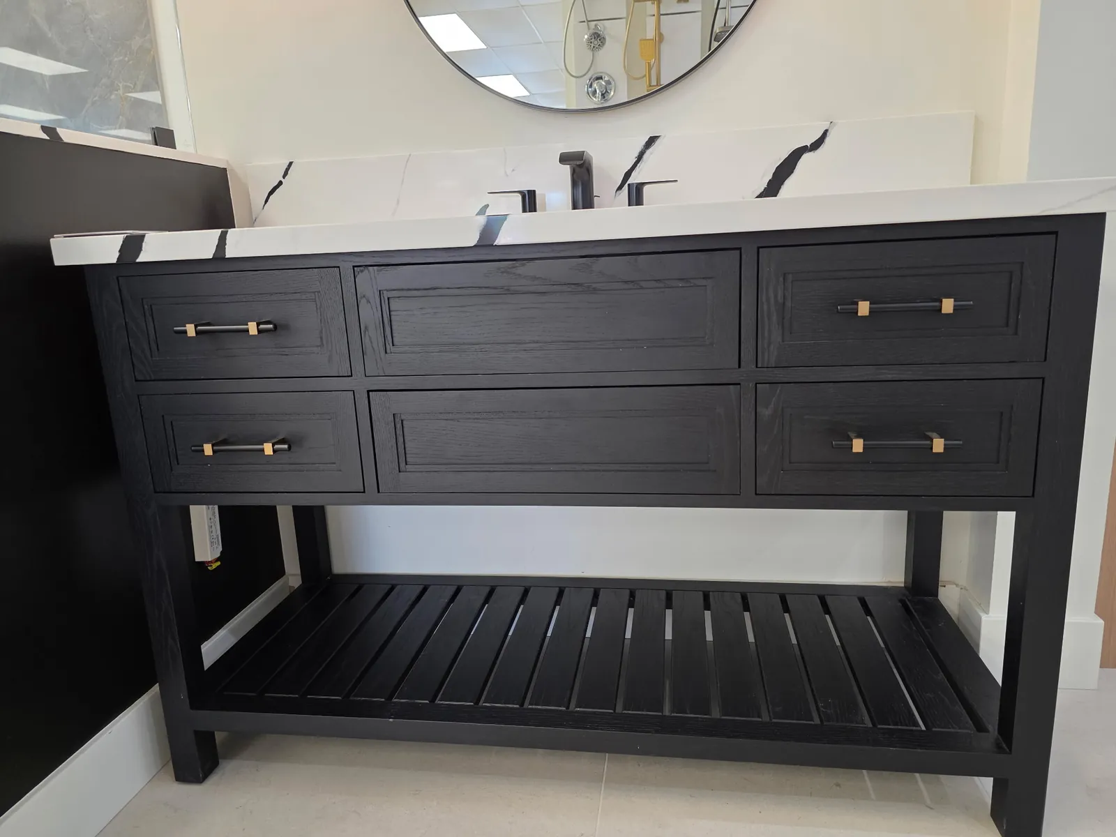 Shiloh Scottsdale white oak six-drawer vanity in the Ink finish — marble waterfall top, slatted lower shelf, mixed black-and-brass bar pulls, against a black-veined marble back wall