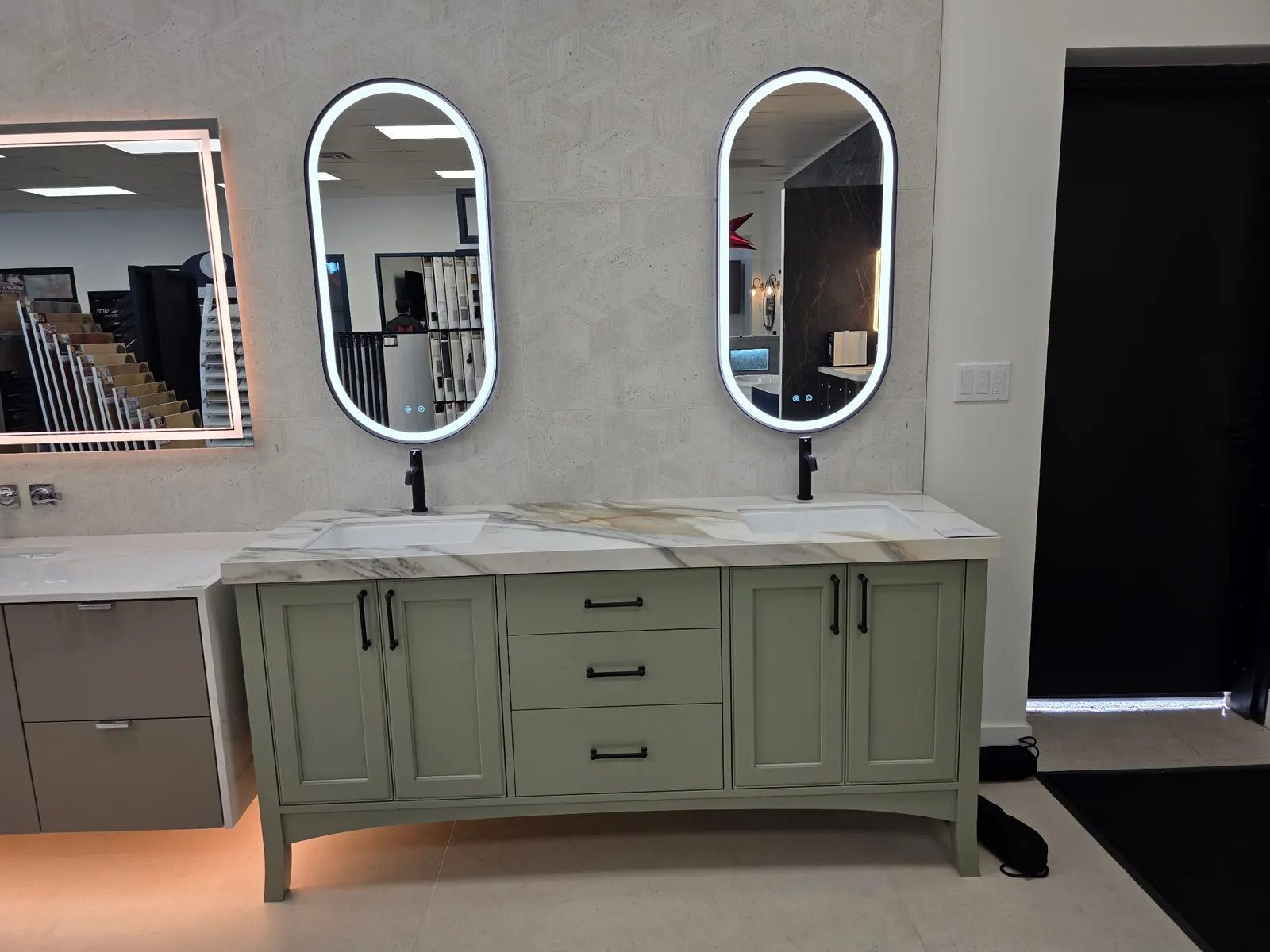 Sage green double-sink vanity on tapered legs, calacatta-style marble counter, oval LED mirrors, black bar pulls