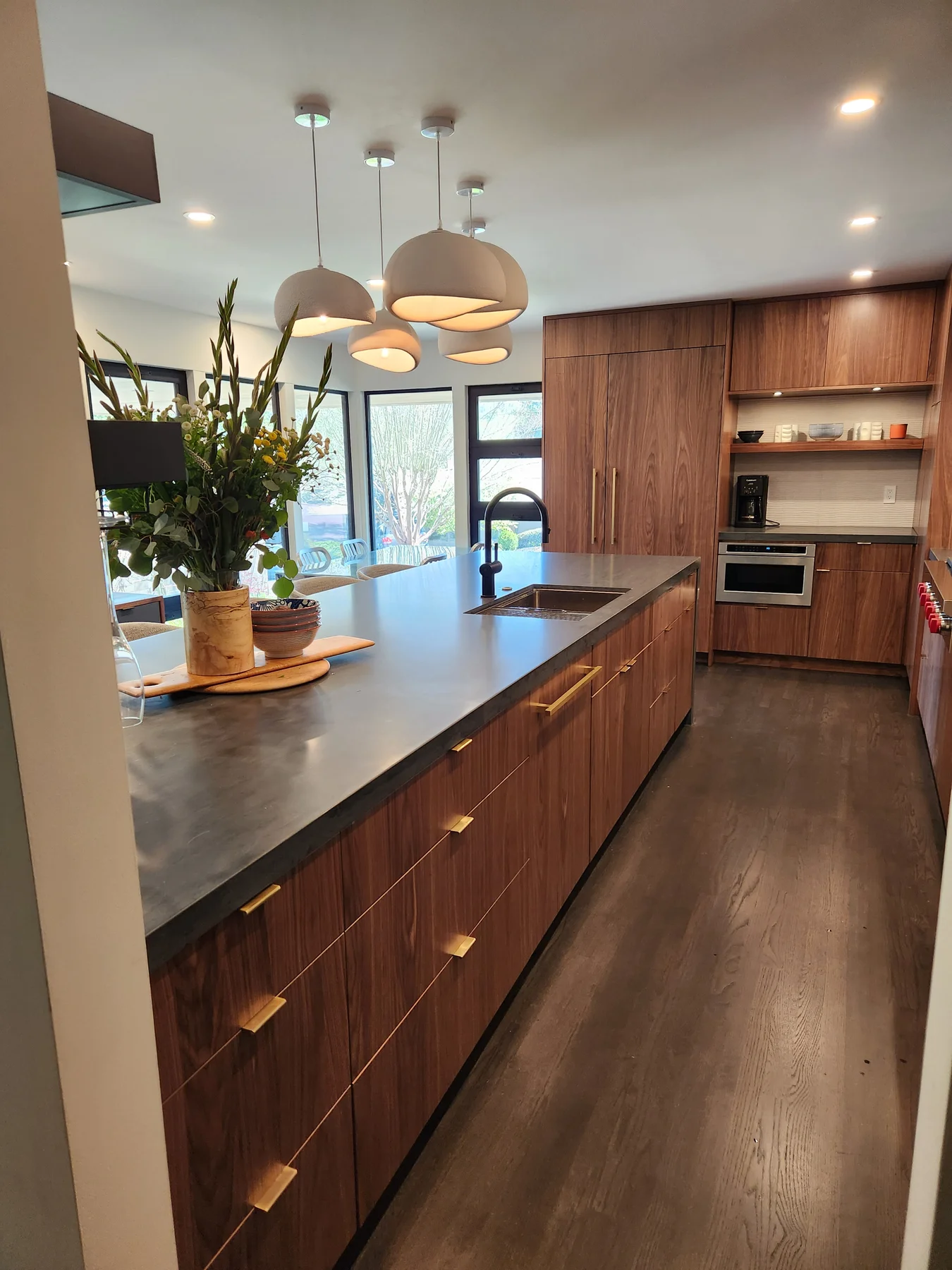 Distinctive Cabinetry Walnut Creek kitchen — long view down the island toward the back of the kitchen with Eclipse Natural Walnut tall pantry and paneled fridge column, a built-in microwave drawer, and a coffee station tucked under wall ovens