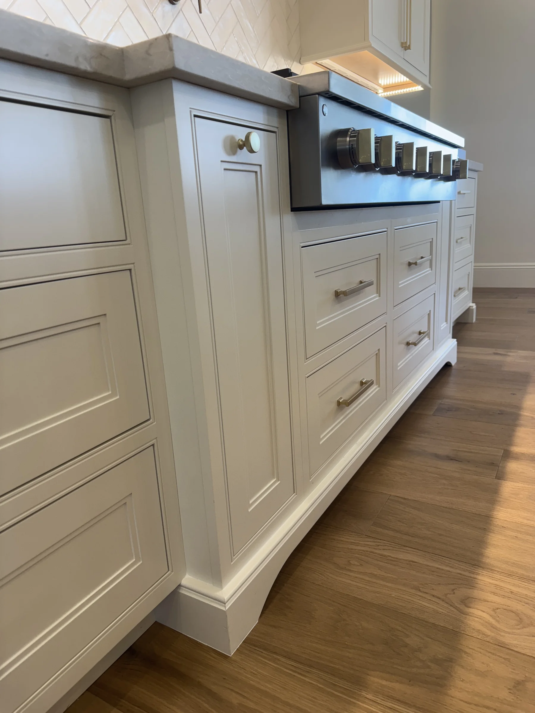 Silverstone Queen Creek kitchen — painted Shiloh inset base detail with brass hardware and Wolf cooktop knobs