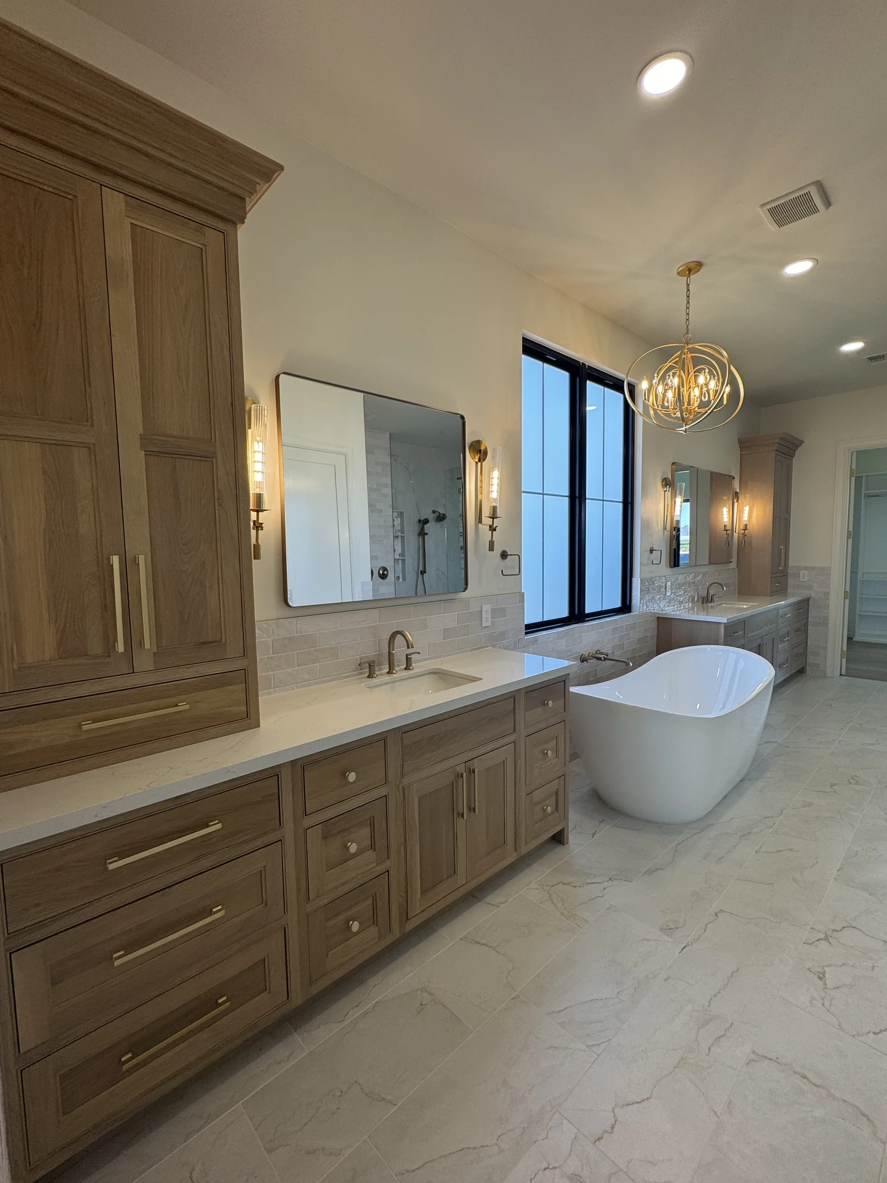 Silverstone Queen Creek primary bath — Shiloh white oak vanities and linen tower with freestanding tub and gold sphere chandelier