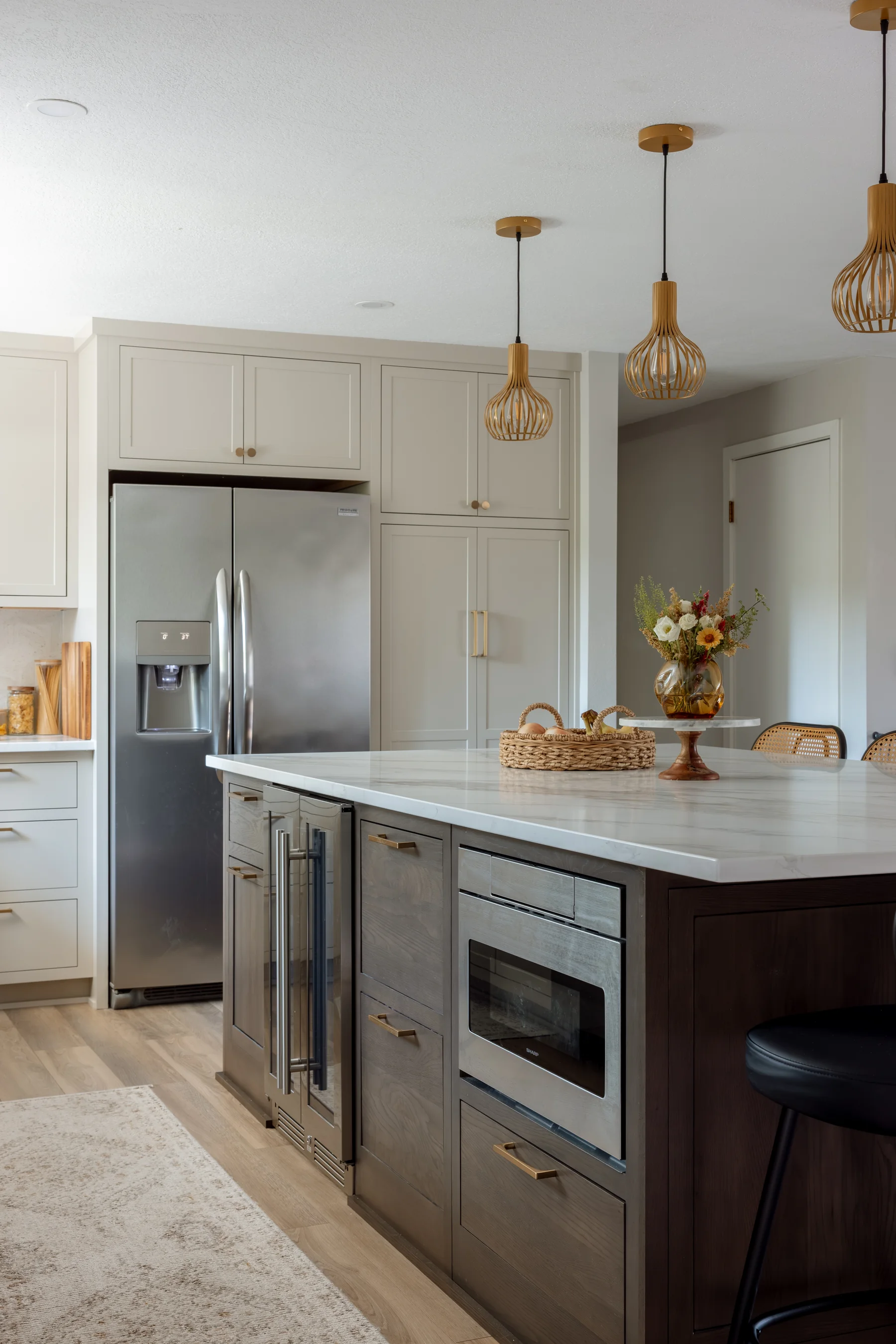 Stutler Cabinets kitchen island — dark stained oak with microwave drawer, glass beverage fridge, and painted pantry tower beyond