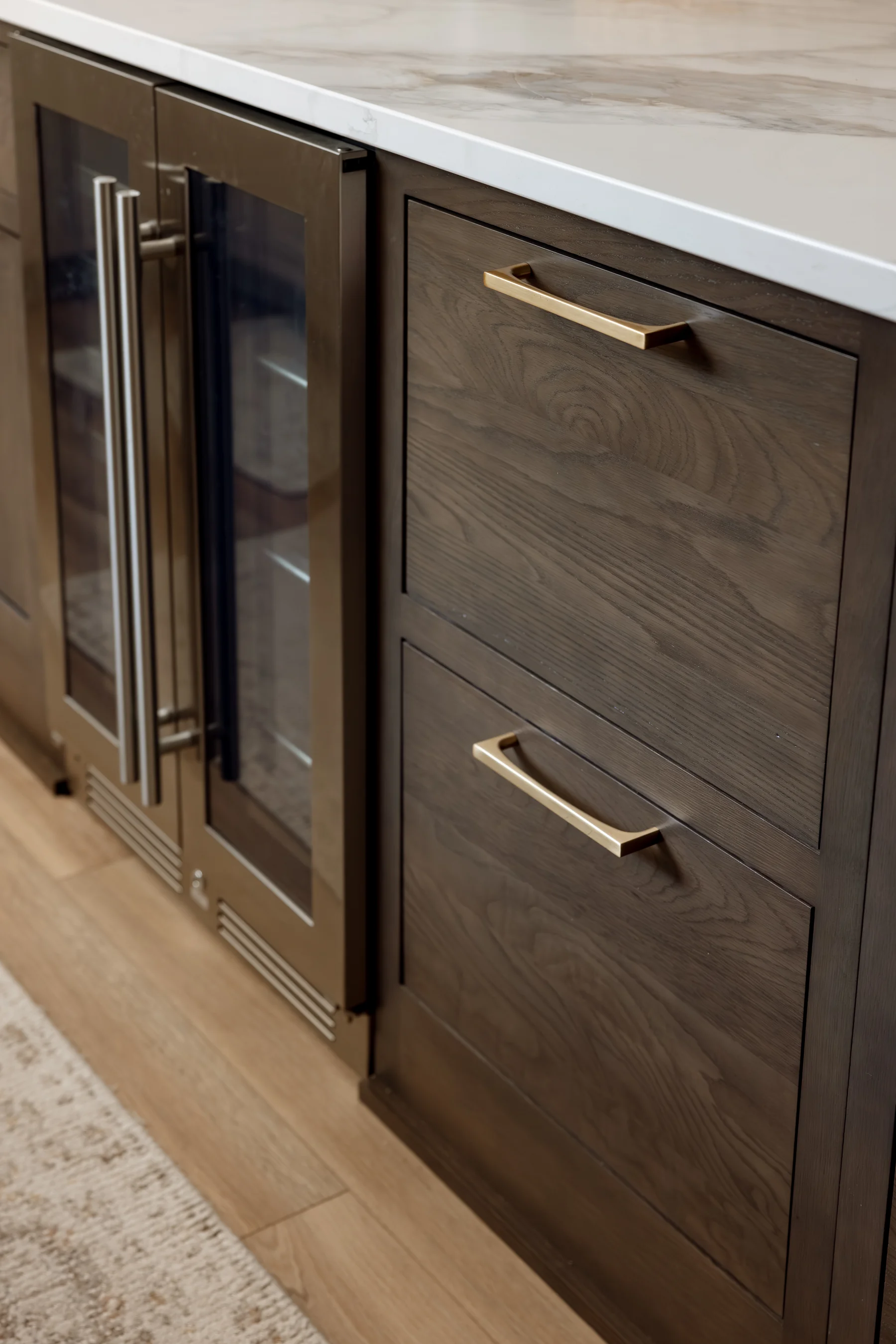 Stutler Cabinets kitchen — close detail of dark stained oak island drawers with brass pulls beside two glass beverage refrigerators
