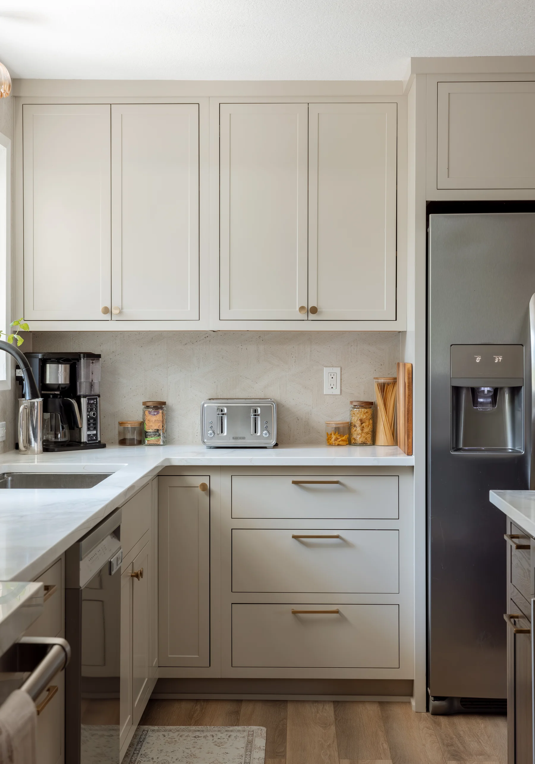 Stutler Cabinets kitchen — painted Shaker perimeter run with brass cup pulls, herringbone tile backsplash, and stainless fridge