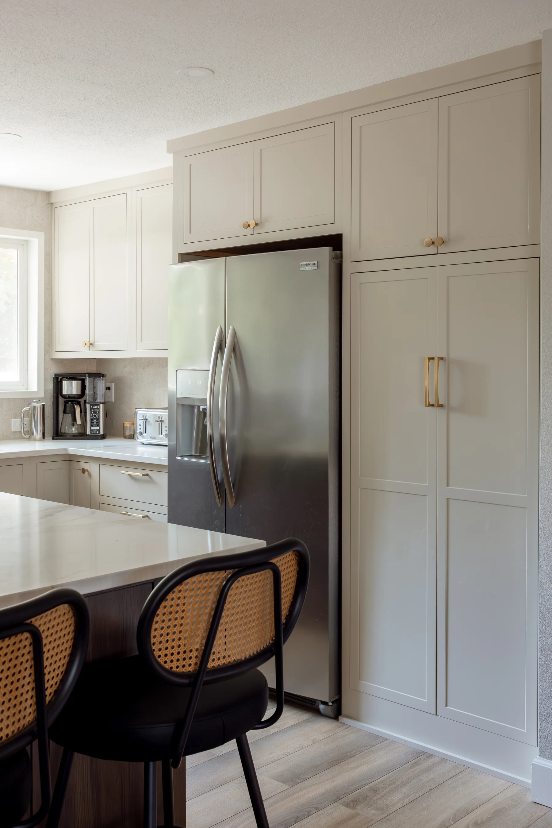 Stutler Cabinets kitchen — full-height painted pantry tower adjacent to the side-by-side fridge, viewed across the dark island