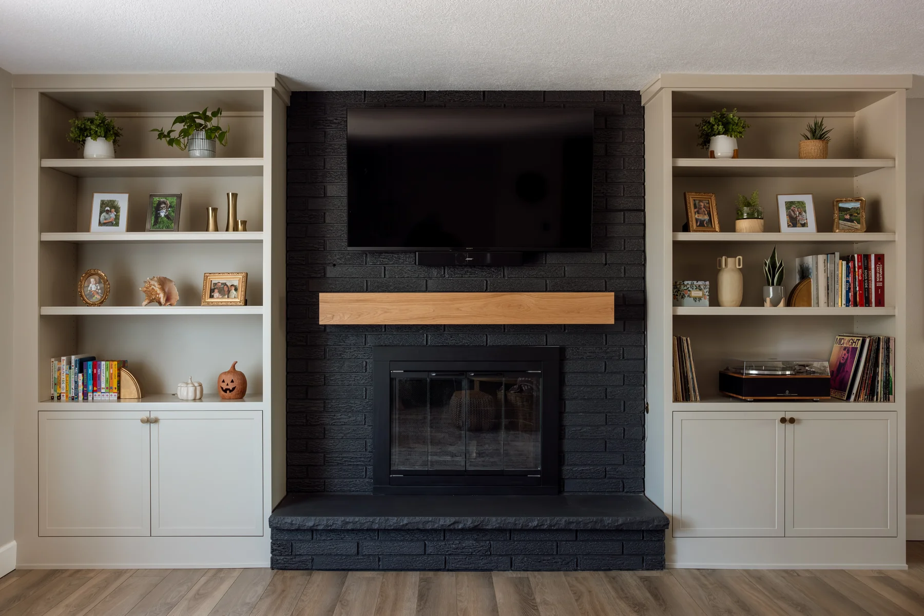 Stutler Cabinets living room — black painted-brick fireplace flanked by white oak mantel and matching painted built-ins on both sides