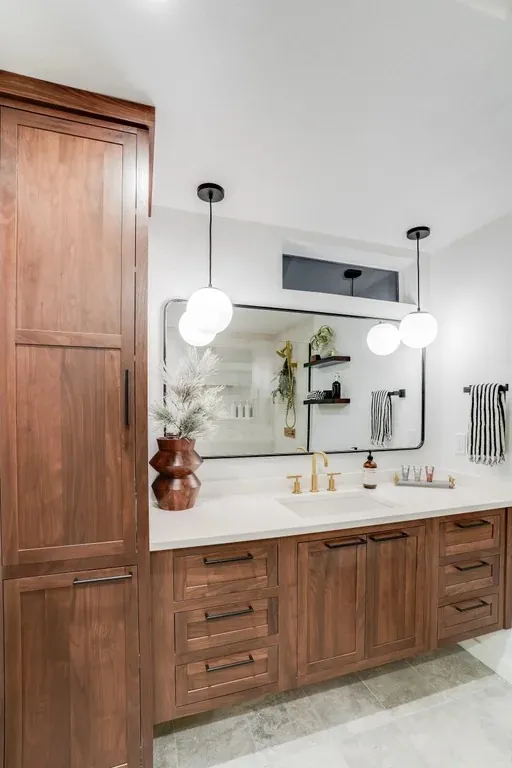 Stutler Cabinets master bath — wide view with tall walnut linen tower and double-sink vanity in Shiloh Malibu walnut Rye, framed mirror and globe pendants