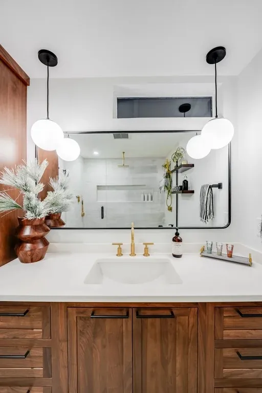 Stutler Cabinets master bath — single sink detail with brass faucet, globe pendants, and walnut Malibu flush-inset cabinetry below